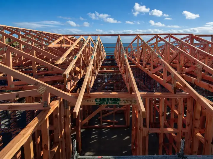 Mo Street — a new house framed and trussed on its platform above the coast, safety netting strung between the trusses and the sea beyond