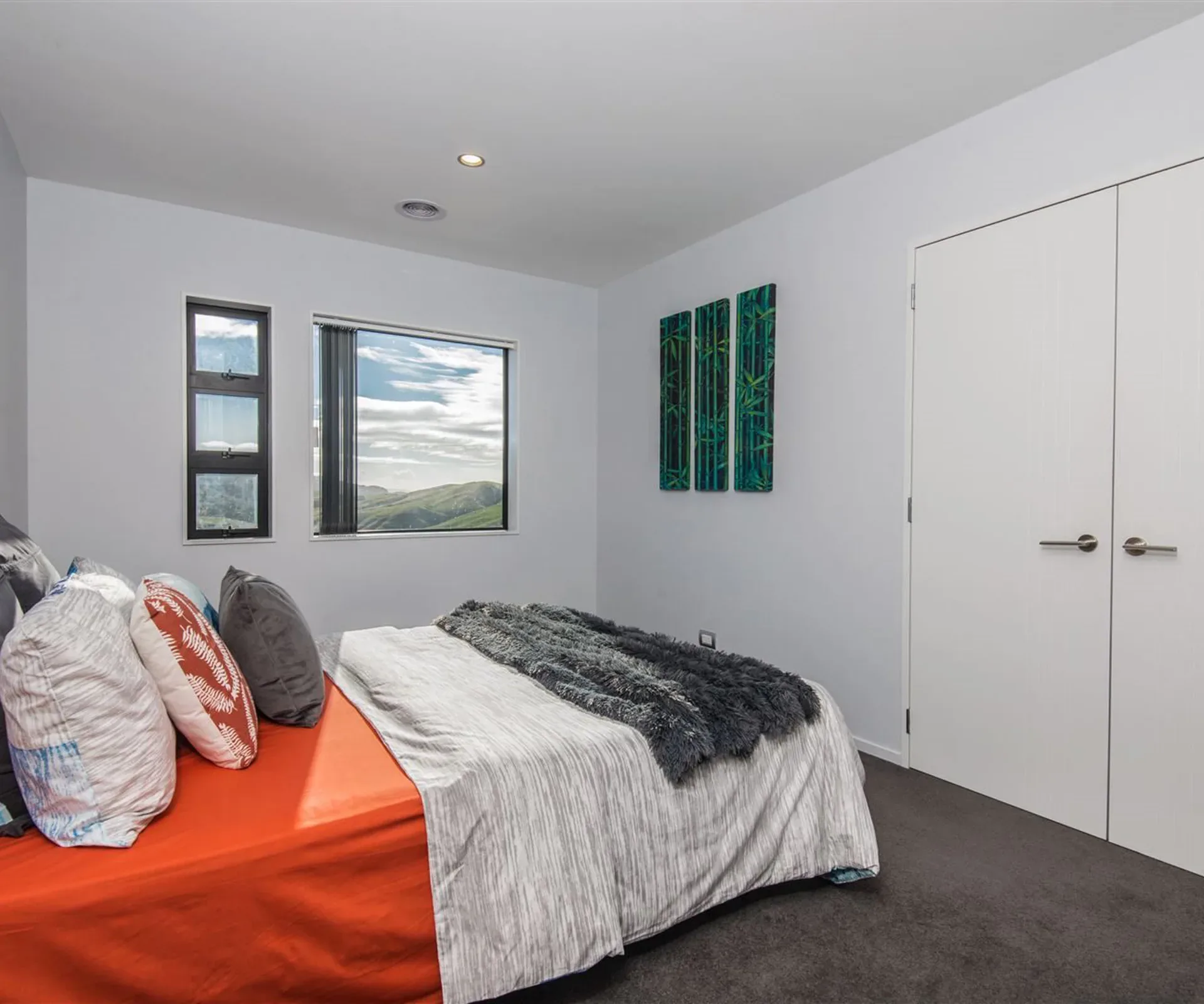 A bedroom with an orange cover on the bed and green bamboo panels on the wall, its corner windows onto the hills and the wardrobe doors alongside.