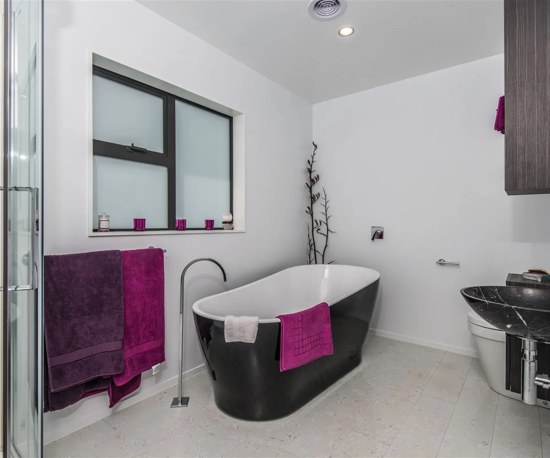 The ensuite — a black freestanding bath with a floor-mounted filler, a glass shower alongside it, and a window above the vanity.