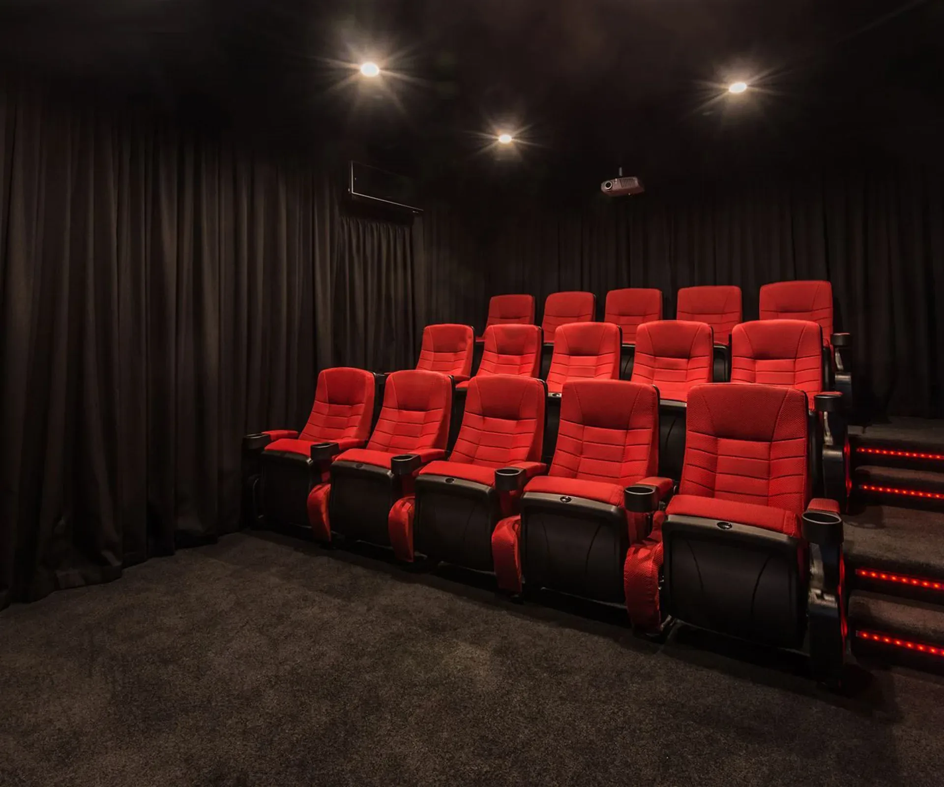 The home theatre — three tiered rows of red recliners facing a curtained wall, with LED strips lighting the steps beside them.