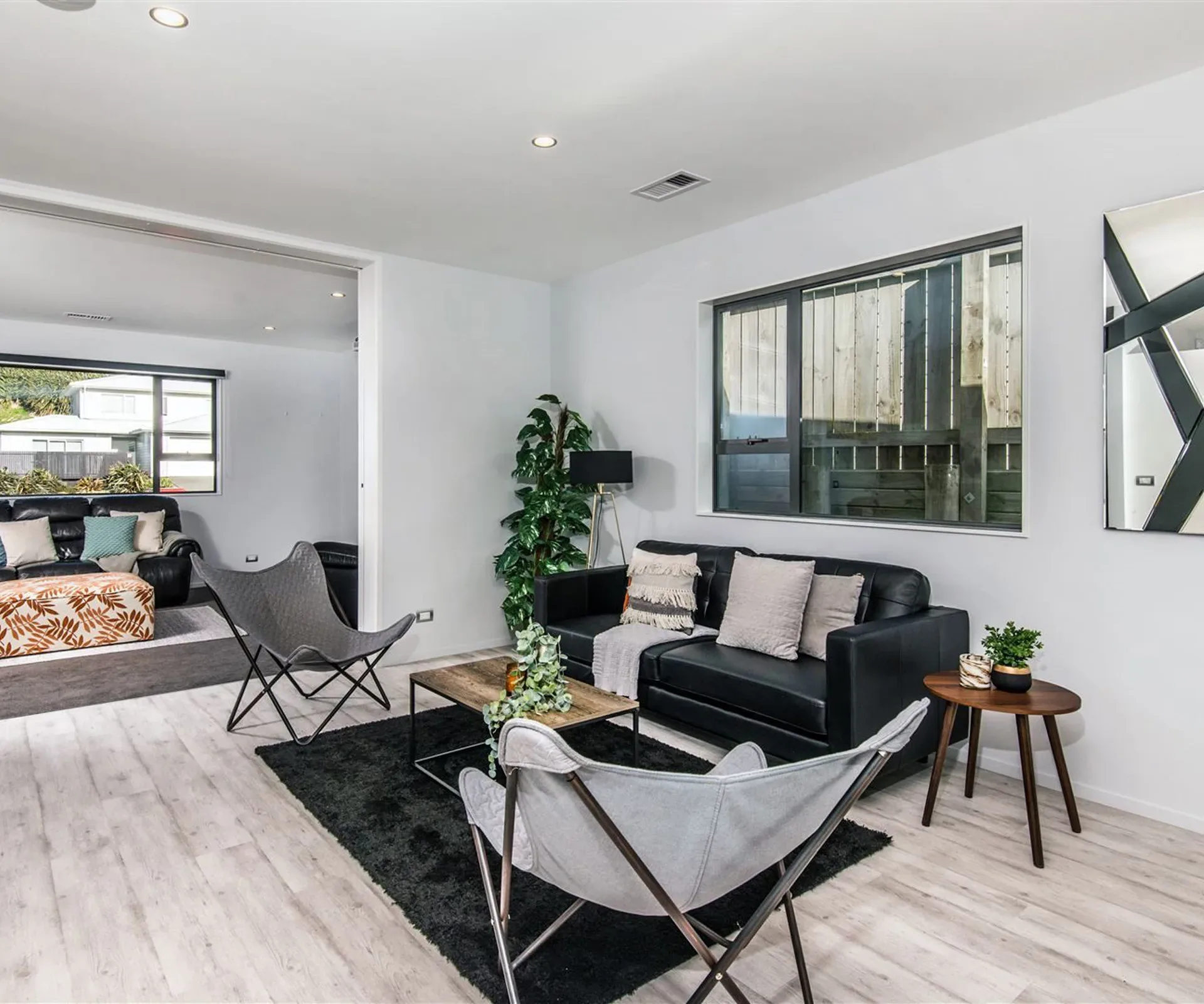 A living space with a wide full-height opening in the wall beside it, the second lounge and its dark leather suite visible through the opening.