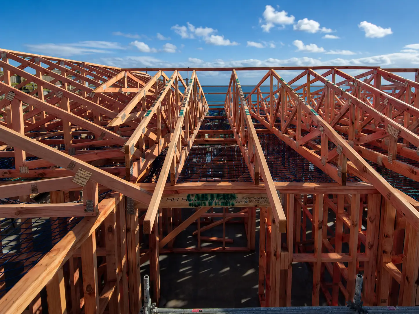 Mo Street — a new house framed and trussed on its platform above the coast, safety netting strung between the trusses and the sea beyond
