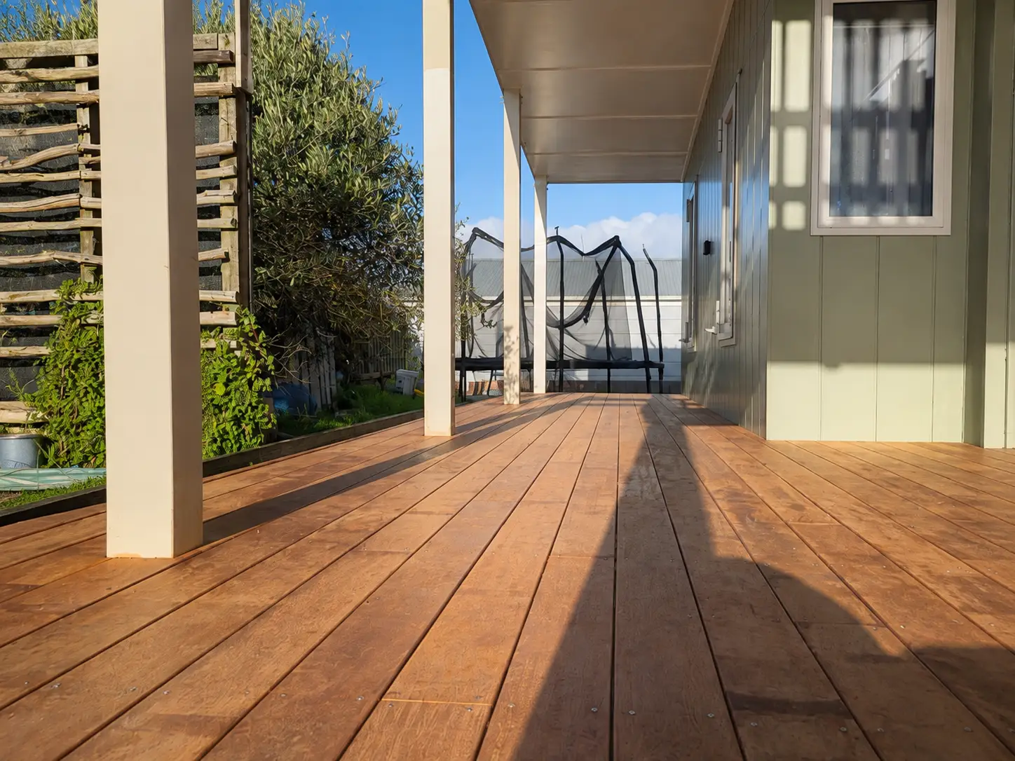 The deck from board level — the run of kwila filling the frame to the far end, every board landing on the same line, with the posts and the garden to the left.