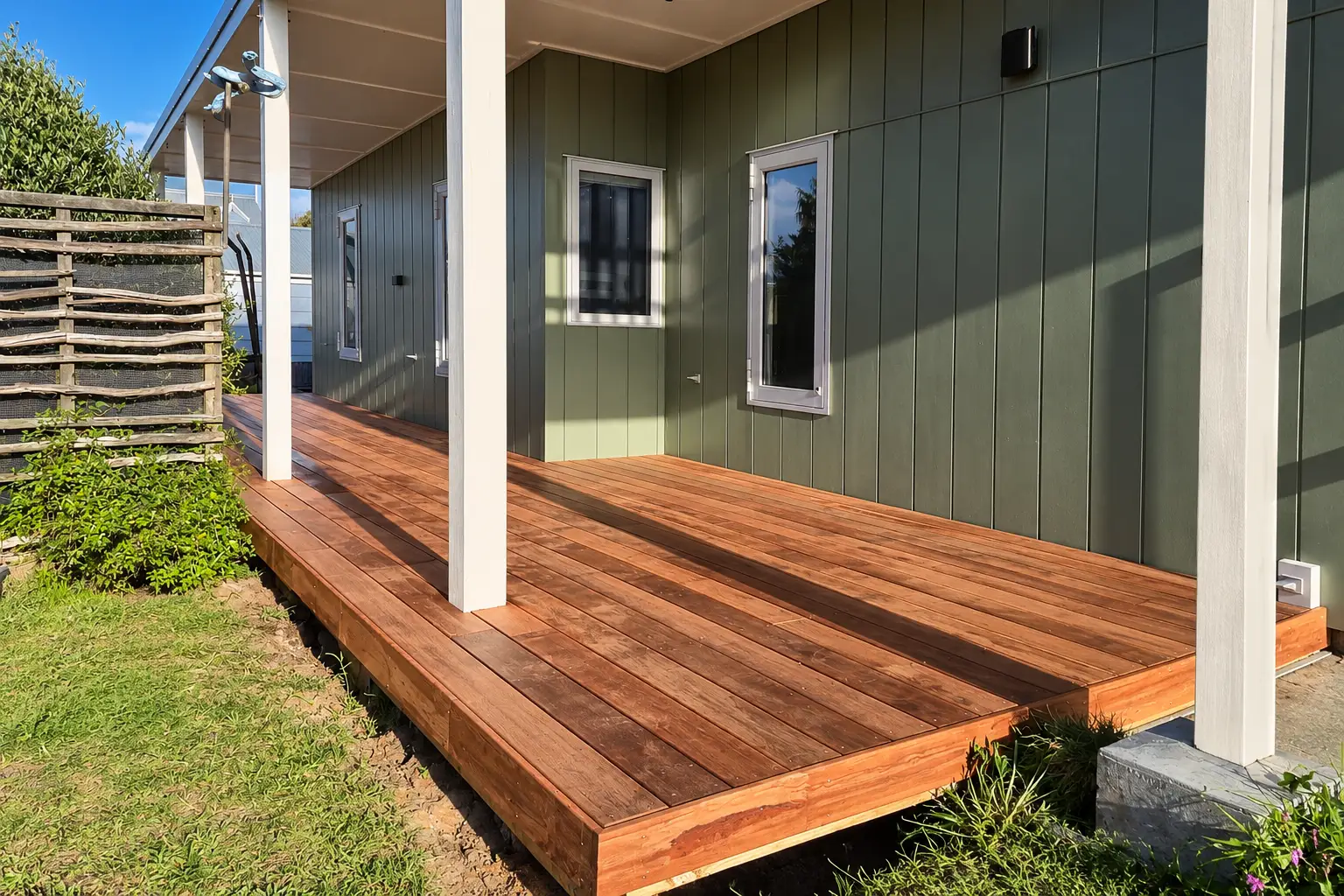 Ollie's Deck — the finished kwila deck from the lawn, running the length of a green board-and-batten wall under a veranda roof