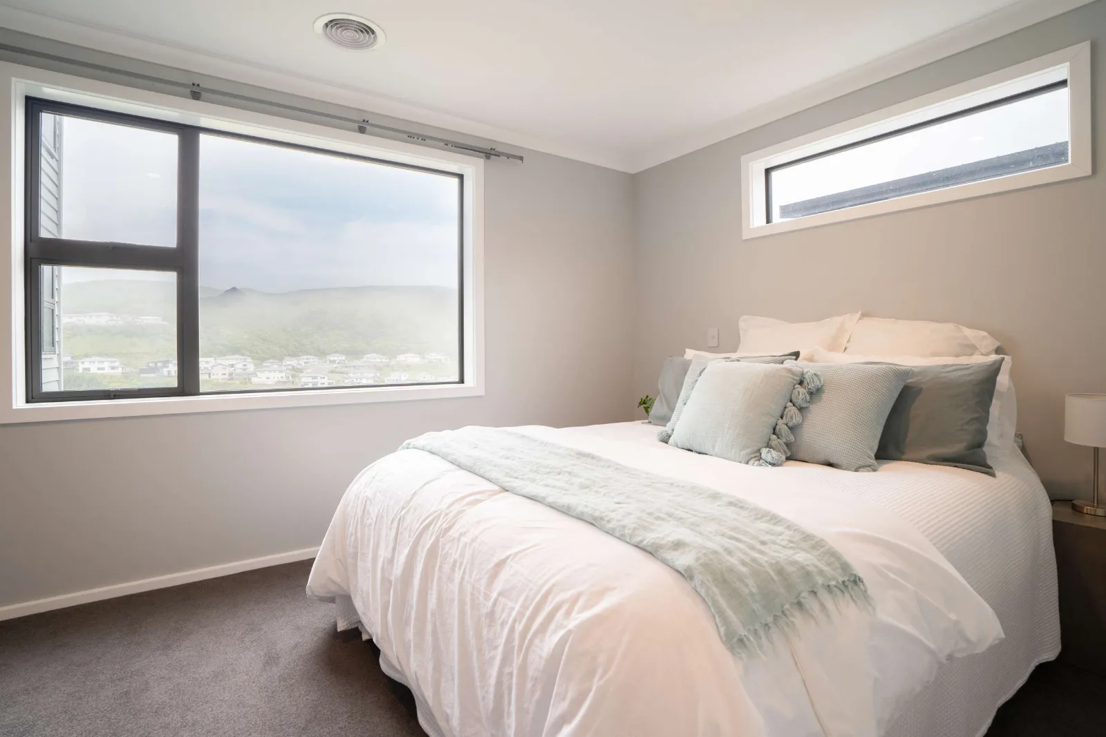 A bedroom with a picture window onto the hills and houses and a narrow high window on the return wall above the bed.
