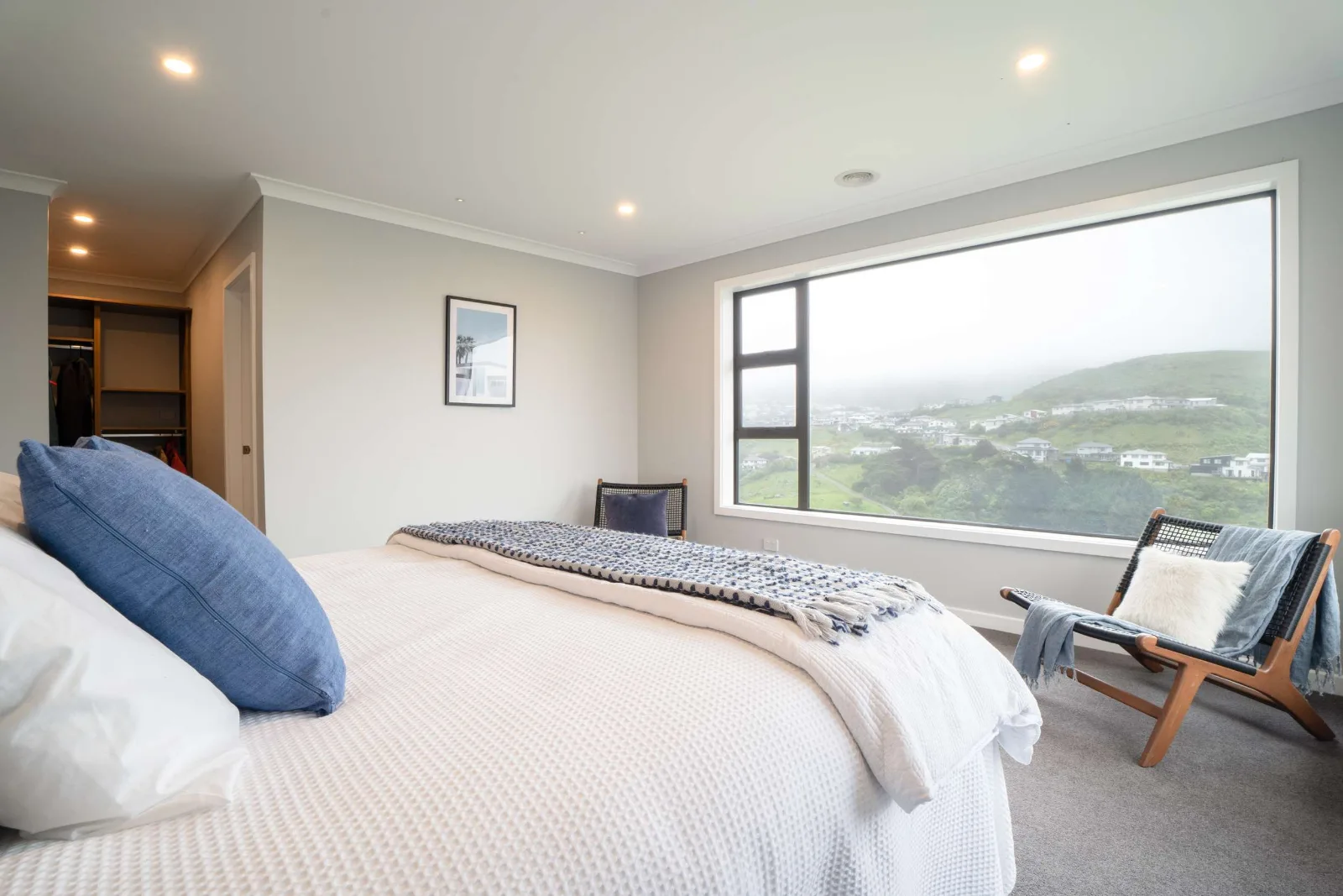 A bedroom with the valley in the window beside the bed and the wardrobe run open to the left.