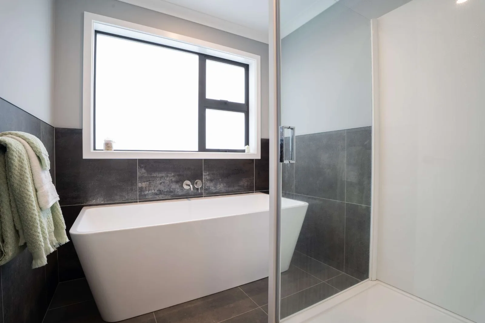 The freestanding bath set against the tiled half-wall under the window, the shower screen returning beside it.
