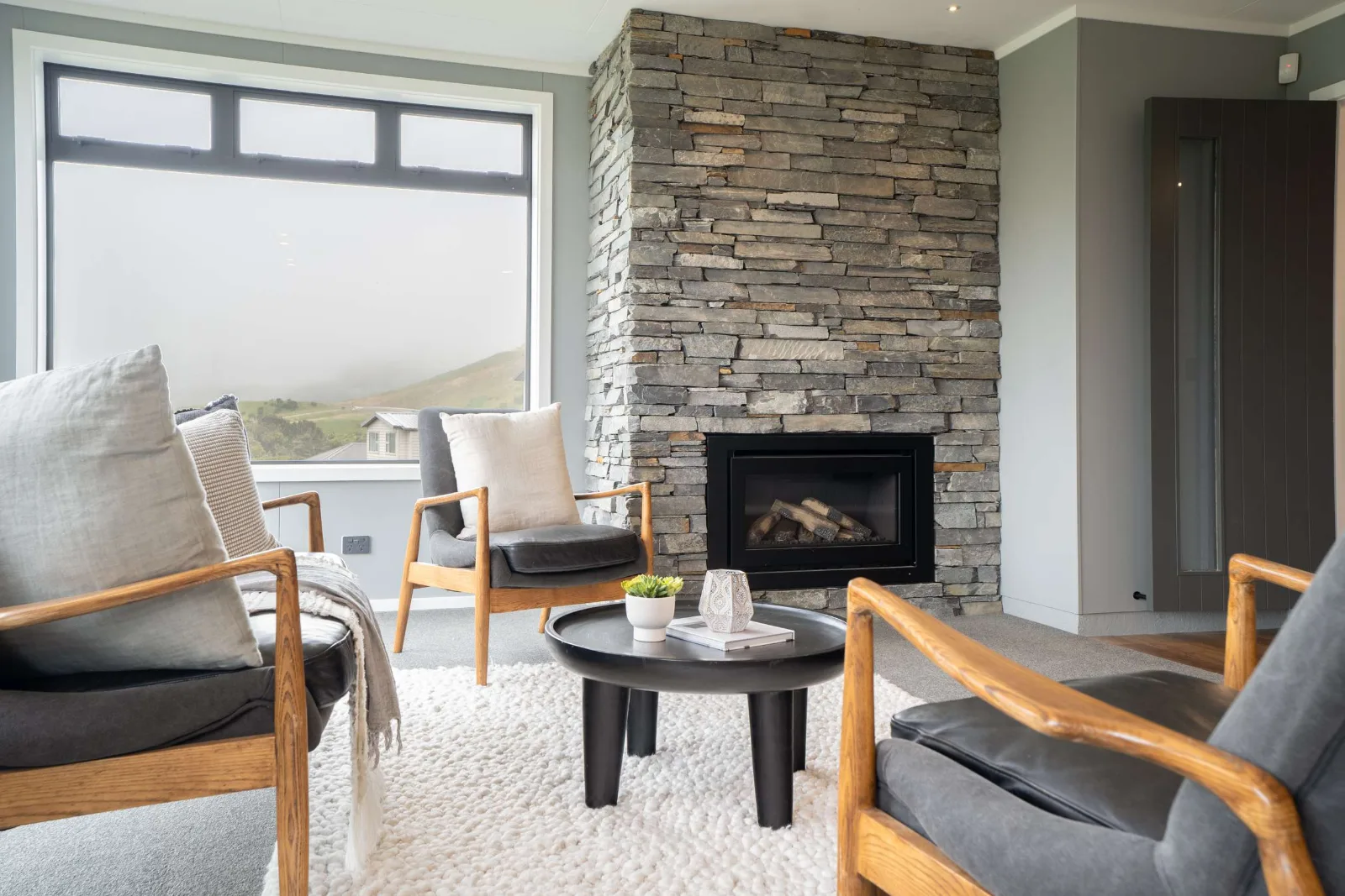 Looking across the seating to the schist chimney breast from the other side, the gas fire set into it and a dark timber door on the return wall.