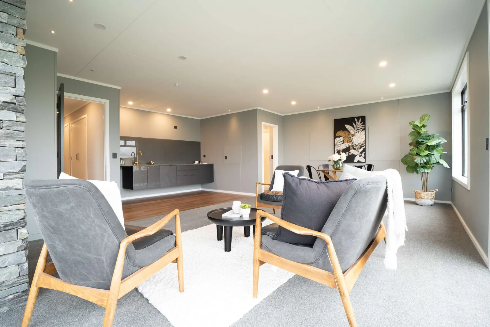 The lower-level living area — chairs on a rug in the foreground and, past the step up, the dark kitchen run and dining table of the second living space.