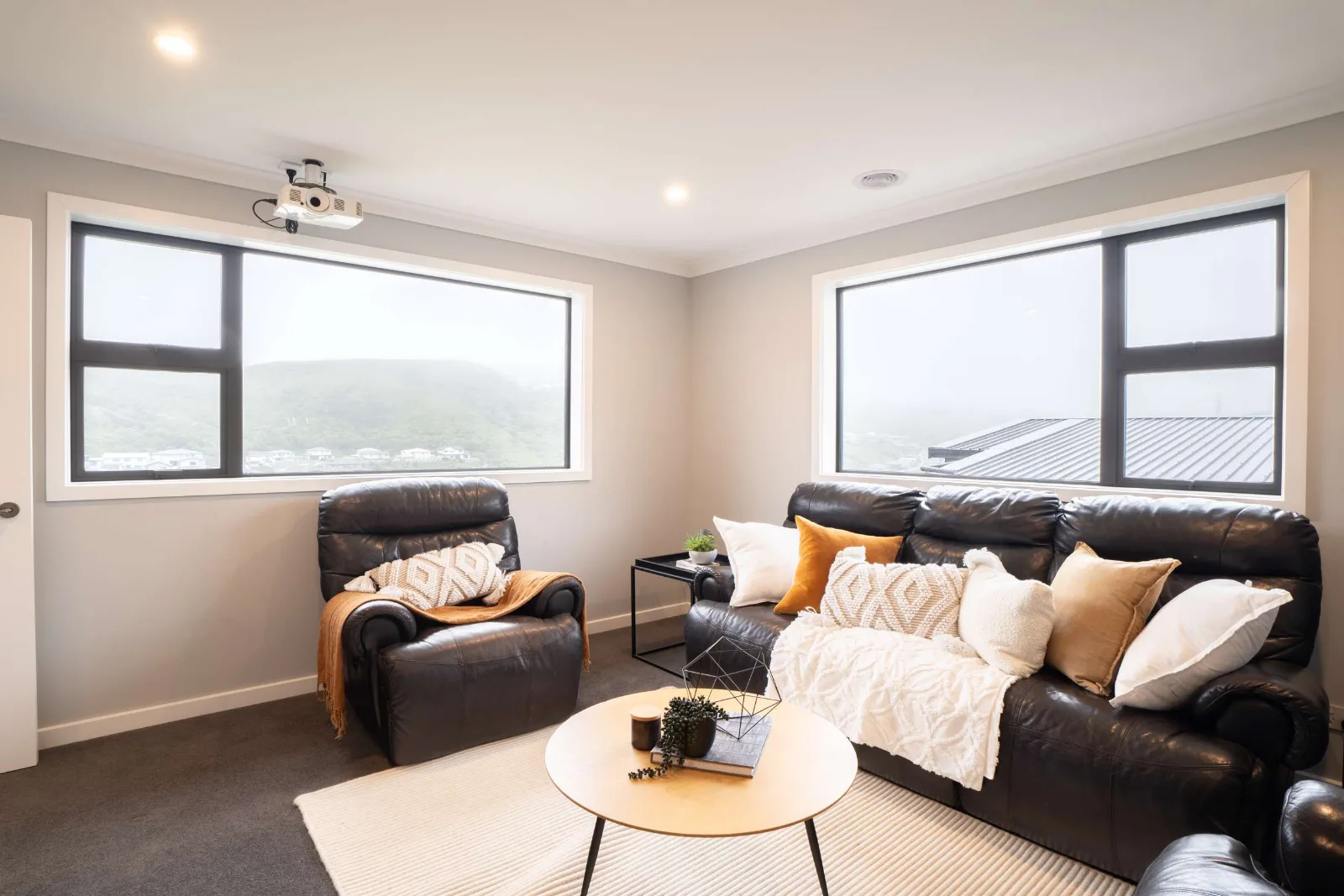 The media room — leather recliners around a low round table, the projector mounted on the ceiling, and two runs of window onto the hills.