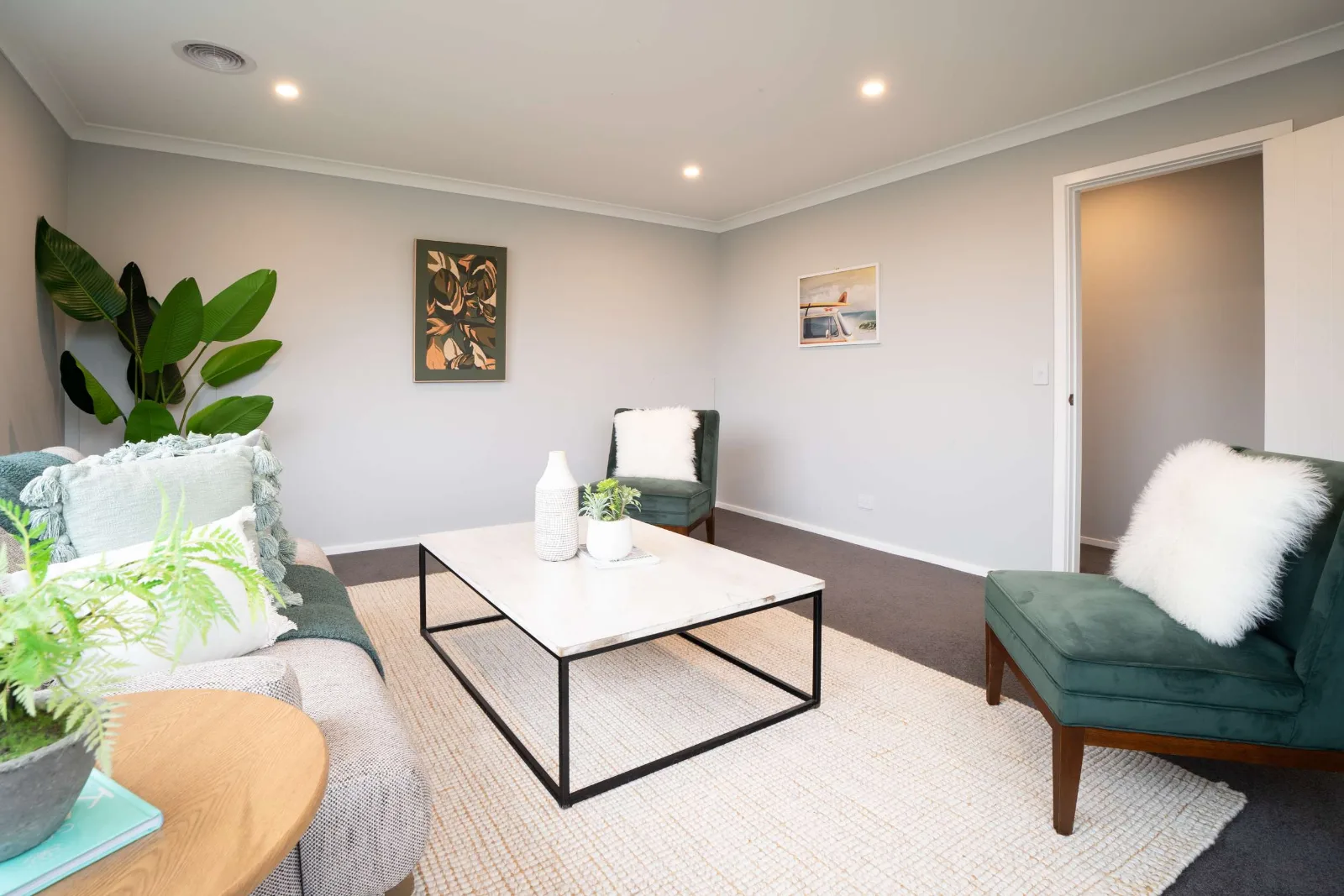 A second sitting room — a linen sofa and two green velvet chairs around a marble-topped table, prints on the walls and a doorway through to the hall.