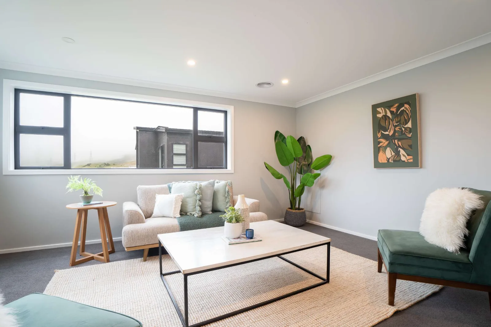 The sitting room's long window onto the neighbouring roof and the hills, the sofa under it and a tall plant standing in the corner.