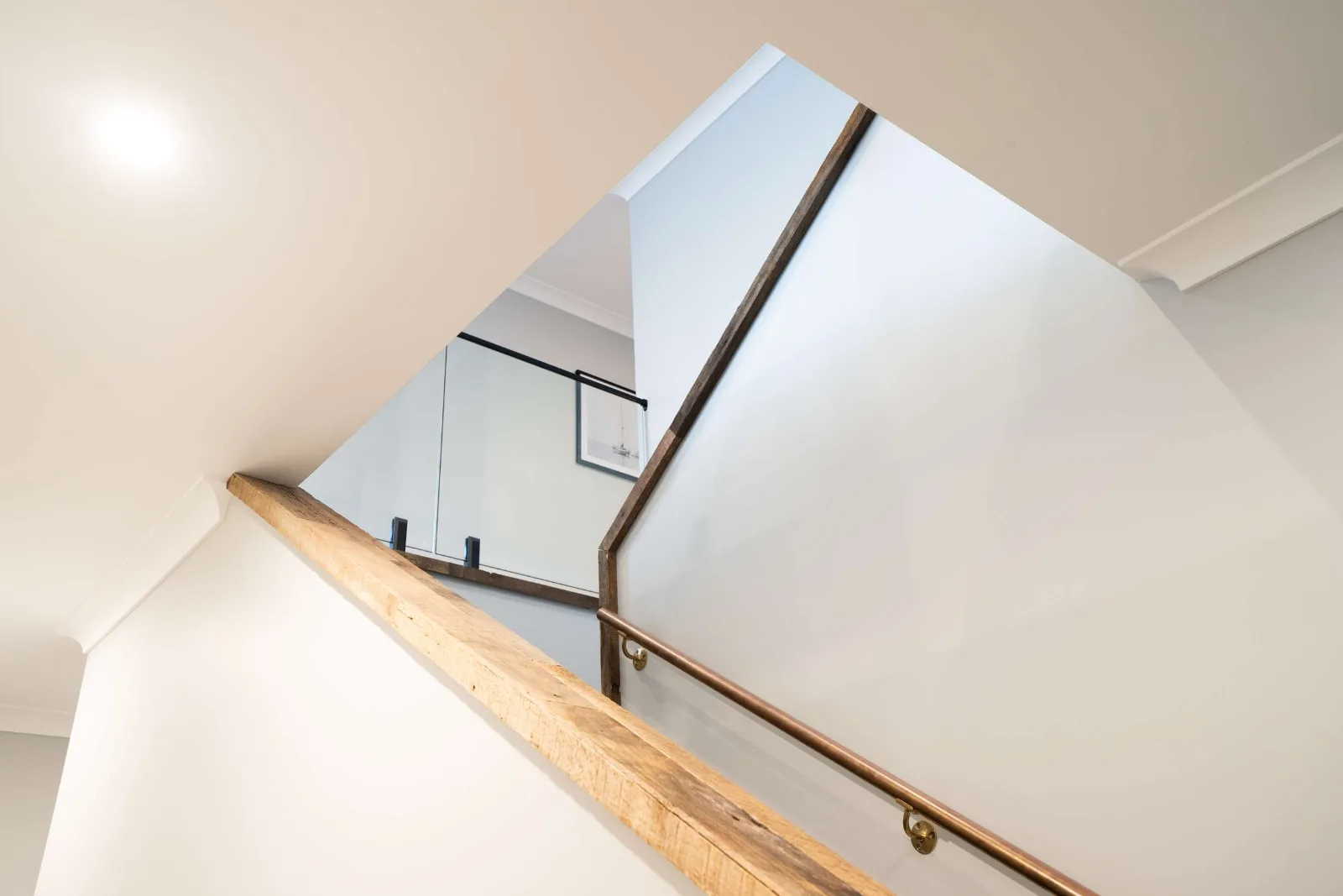 The stair from the flight below — the recycled-oak capping running unbroken around the turn of the glass balustrade, its bracket fixings set into the glass.