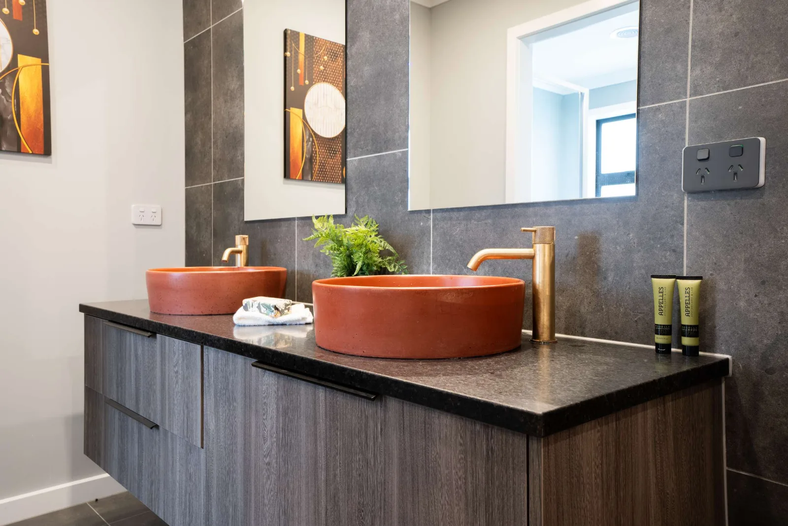 Two terracotta vessel basins on a dark stone top, each with its own brass tap, under separate mirrors on the tiled wall.